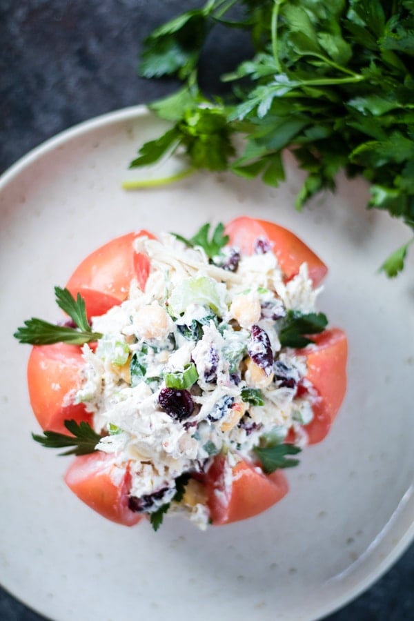 Mayo free Chicken salad stuffed inside of a heirloom tomato on a plate with parsley on the side.