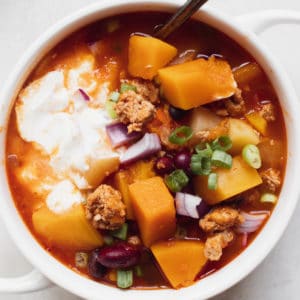 chili in a white soup bowl topped with green onions and sour cream