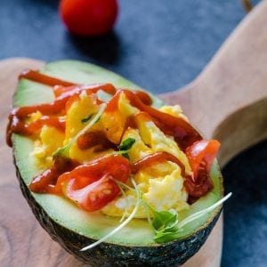 Scrambled eggs in an avocado topped with tomatoes and Sriracha