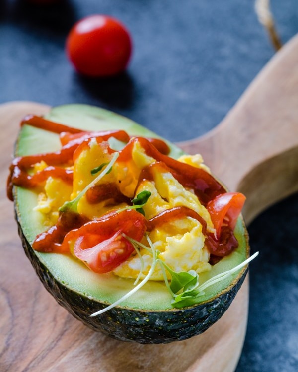 Scrambled eggs in an avocado topped with tomatoes and Sriracha