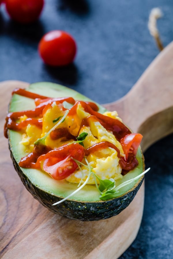 Scrambled eggs in a avocado topped with tomatoes and Sriracha