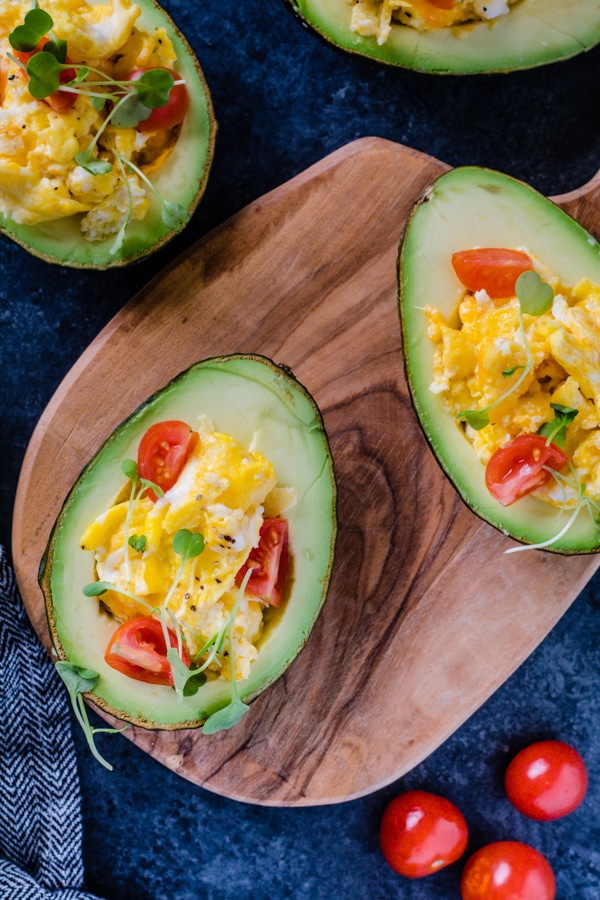 Scrambled eggs in a avocado topped with tomatoes 
