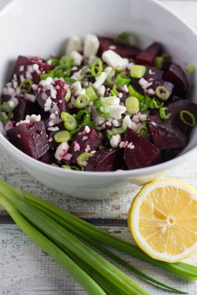 Chopped roasted beets on a wood board topped with feta cheese and green onions.