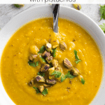 pumpkin soup in a white bowl topped with parslet and pistachios