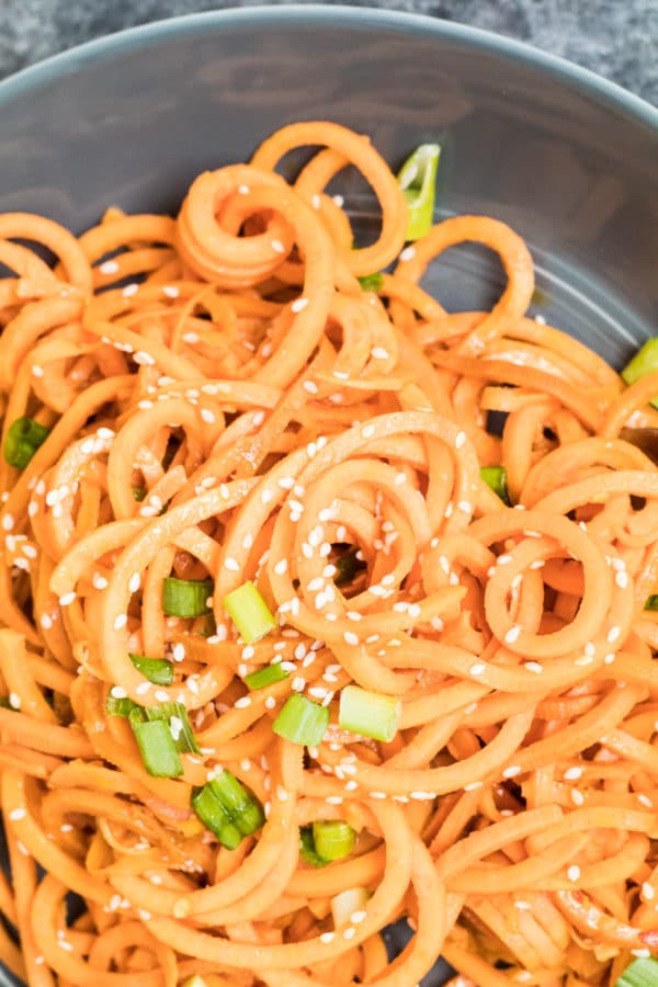 sweet potato noodles in a grey bowl topped with sesame seeds and green onions
