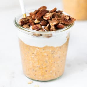 overnight oats made with pumpkin puree in a glass jar topped with Greek yogurt, chopped pecans and ground cinnamon