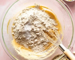 Mixing bowl with partially combined wet ingredients and dry ingredients, including flour, baking soda, and salt, being whisked together to form cookie dough.
