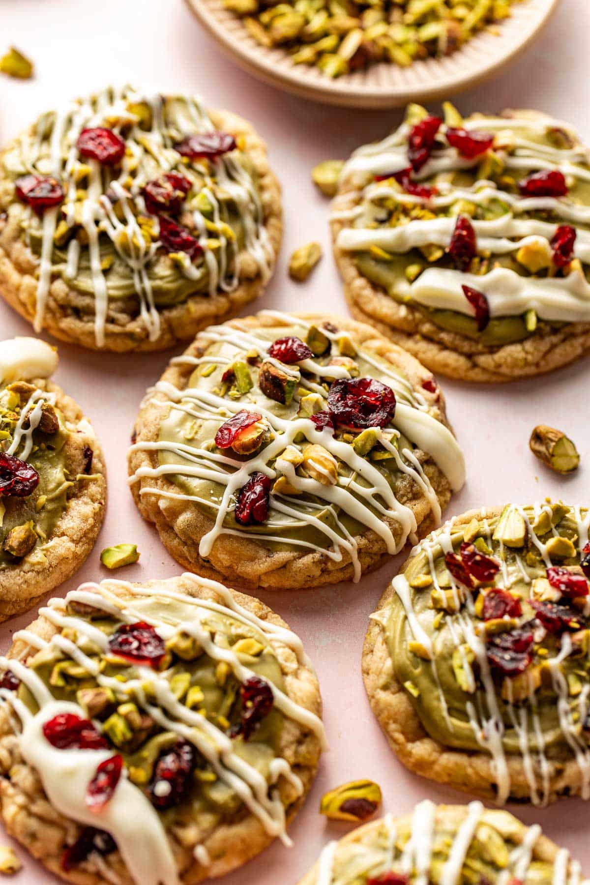 Stack of pistachio cranberry cookies showing a soft, chewy interior with white chocolate chips, pistachios, and cranberries, topped with green frosting and drizzled white chocolate.