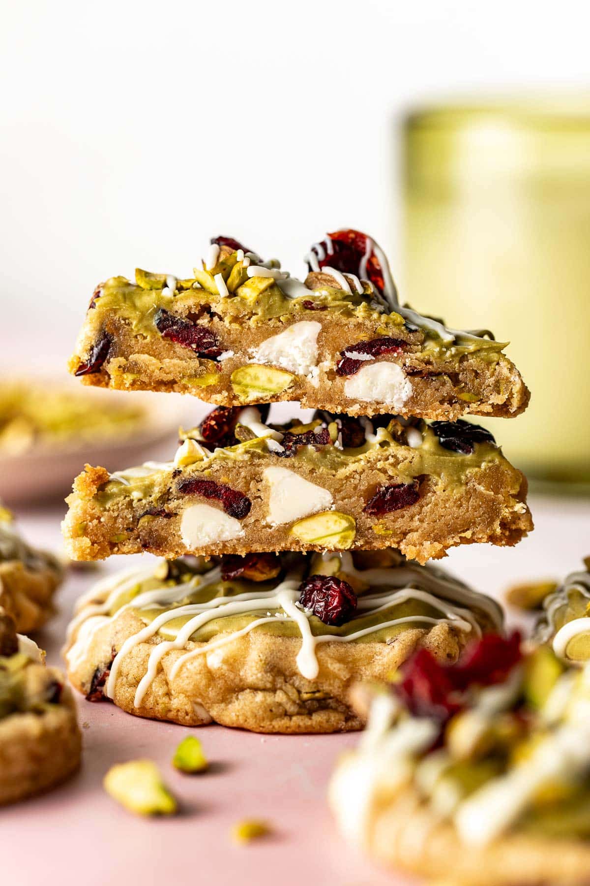 Pistachio cranberry cookies stacked on top of each other, one with a bite taken out, revealing soft centers with cranberries and white chocolate chips.