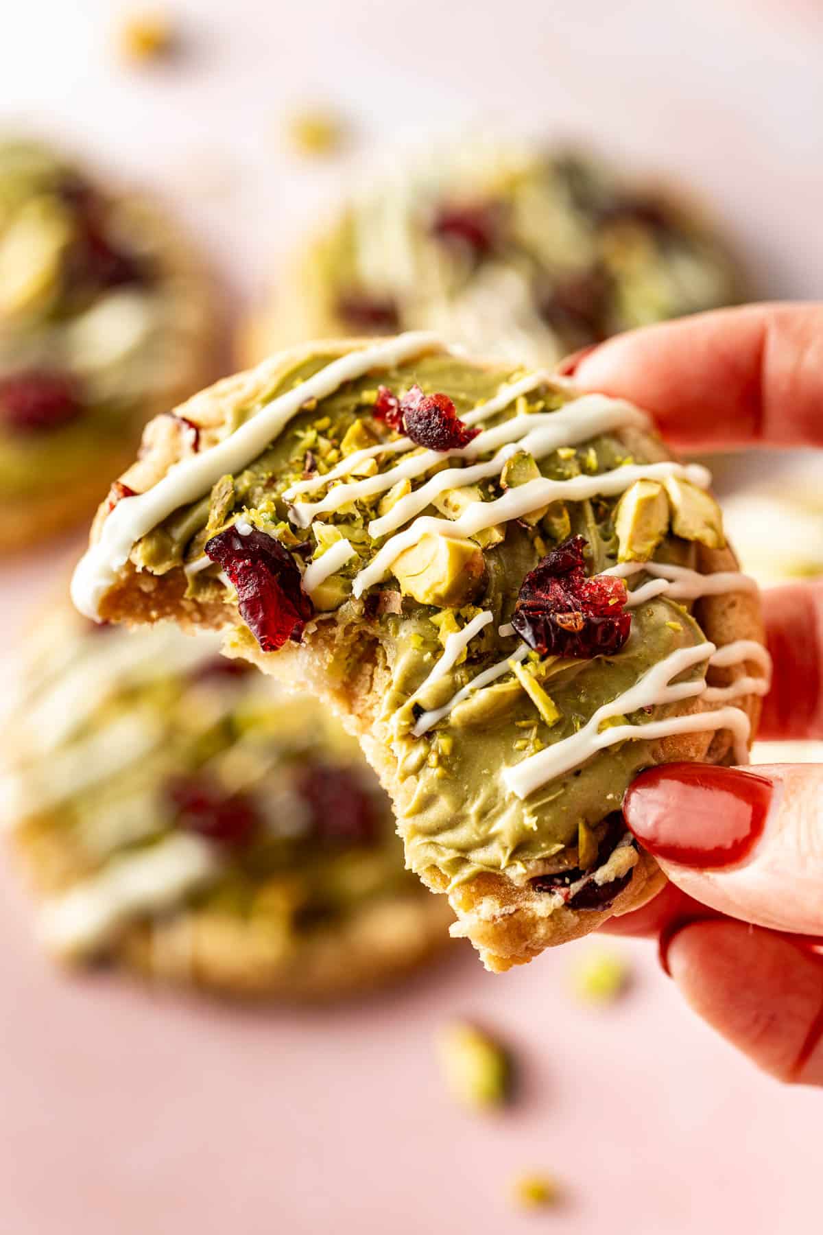Festive pistachio cranberry cookies on a pink background with white chocolate drizzle and bright red cranberries, perfect for the holidays.