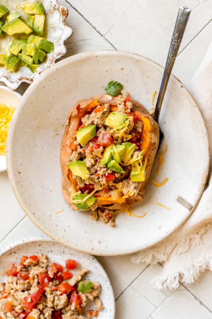 a sweet potato in a bowl stuffed with ground turkey and topped with avocado and cheese