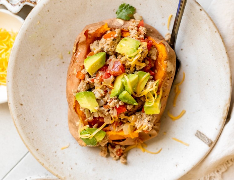 a sweet potato in a bowl stuffed with ground turkey and topped with avocado and cheese