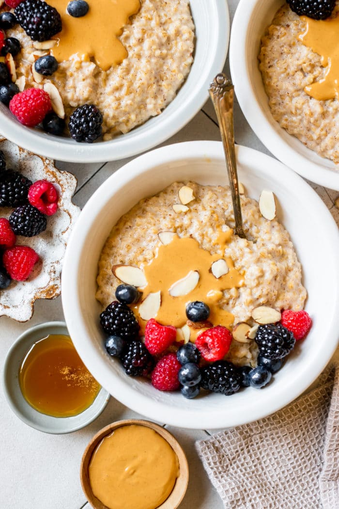 steel cut oatmeal in white bowls topped with peanut butter and fresh berries.