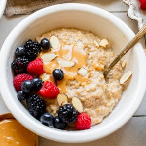 steel cut oatmeal in white bowls topped with peanut butter and fresh berries.