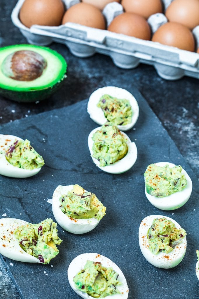 avocado deviled eggs on dark countertop next to avocado half