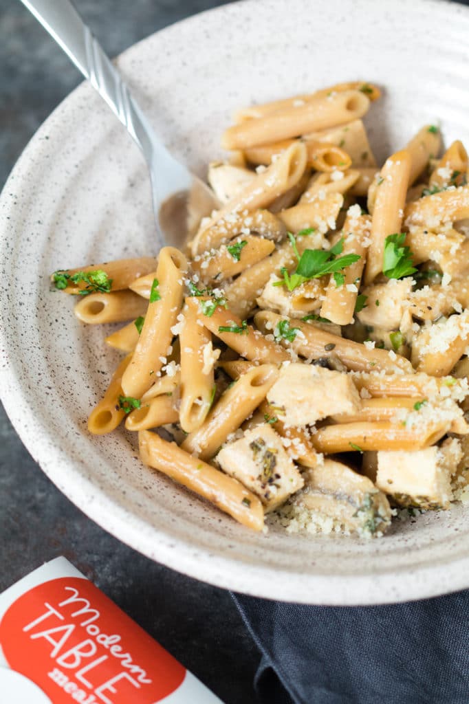 herb pasta in a bowl with chicken and topped with parsley