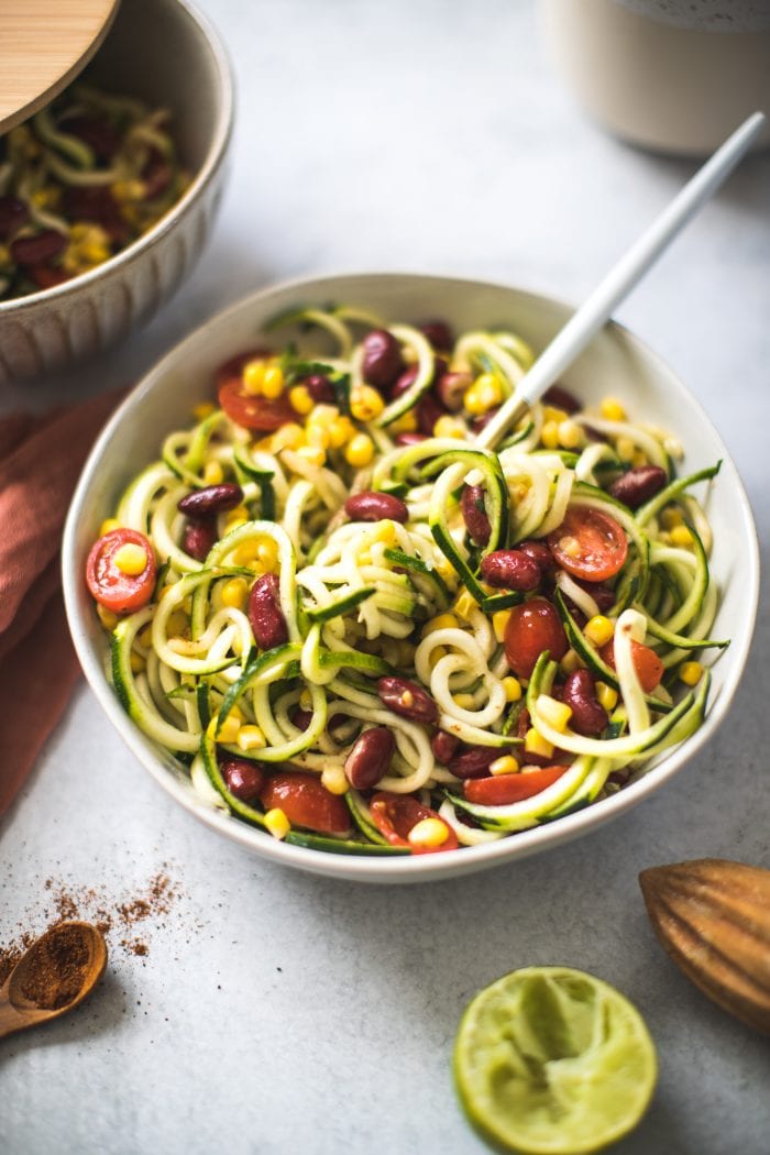 zoodle salad in a large white bowl with corn, tomatoes and kidney beans