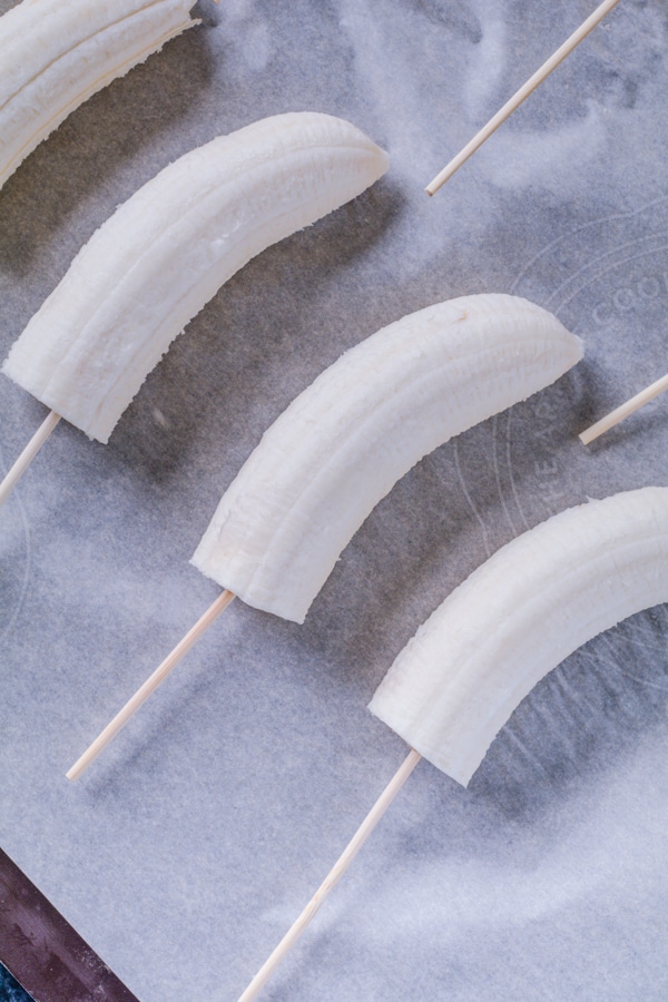 Bananas cut in half on a stick placed on a cookie sheet