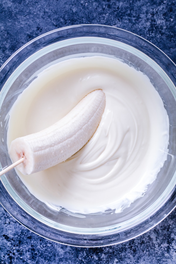 White chocolate melted in a glass bowl with a banana being dipped into it.