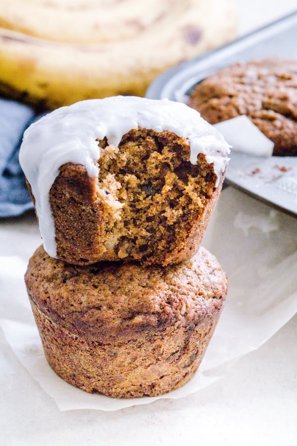 Two muffins stacked on top of each other. Top muffin has frosting on it.