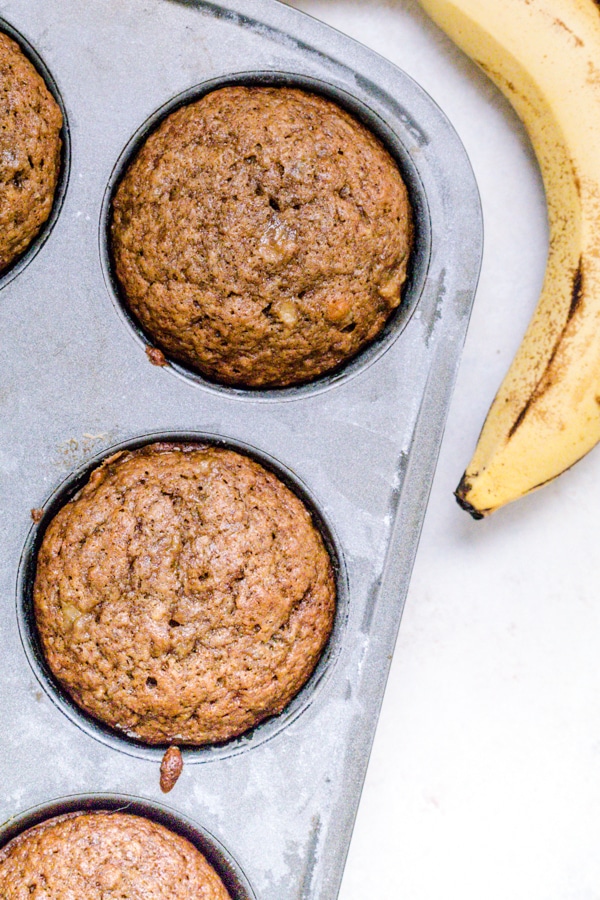 Muffins in a muffin tin with ripe bananas on the side.