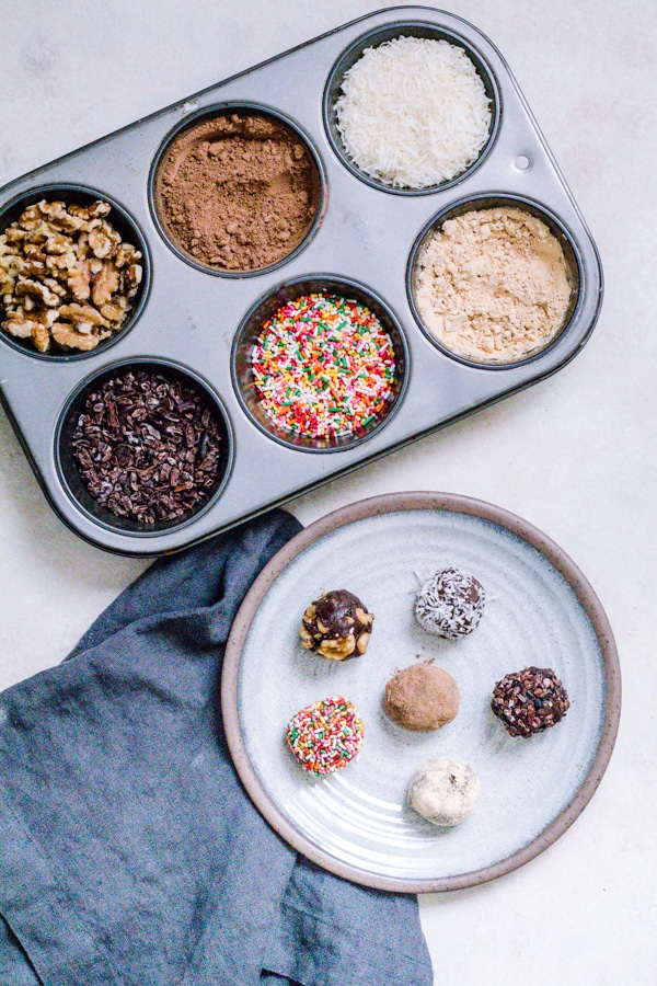 Decorated No Bake Pumpkin Brownie Bites on a plate with the toppings on the side in a muffin tin. 