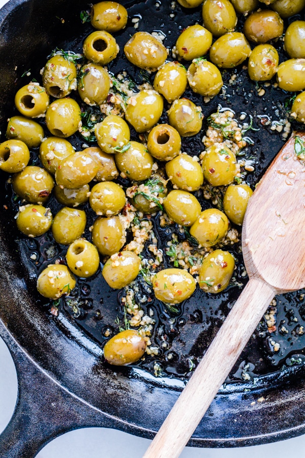 Green olives in a cast iron skillet with fresh garlic and garden fresh herbs