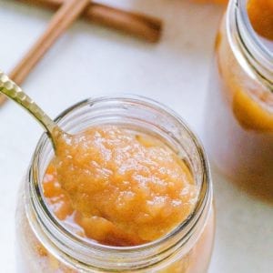 Applesauce made with pumpkin in a mason jar. A spoon is in the mason jar with cinnamon sticks in the background.