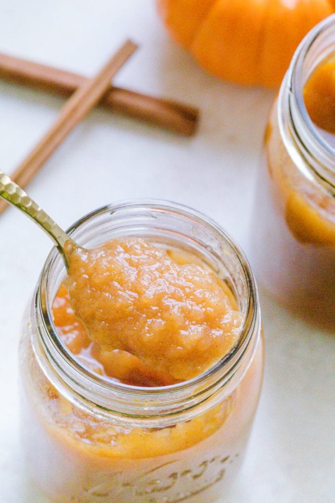 Applesauce made with pumpkin in a mason jar. A spoon is in the mason jar with cinnamon sticks in the background.