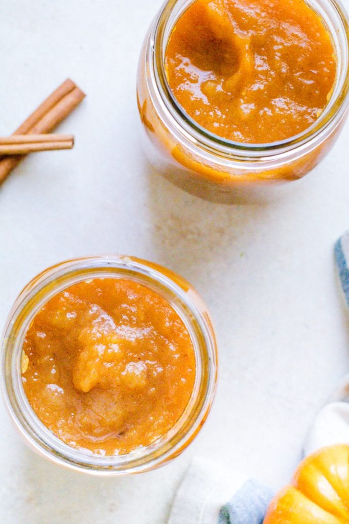 Applesauce made with pumpkin in a mason jar. A spoon is in the mason jar with cinnamon sticks in the background.