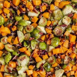 roasted brussels sprouts and butternut squash on a gold sheet pan garnished with chopped pecans and dried cranberries