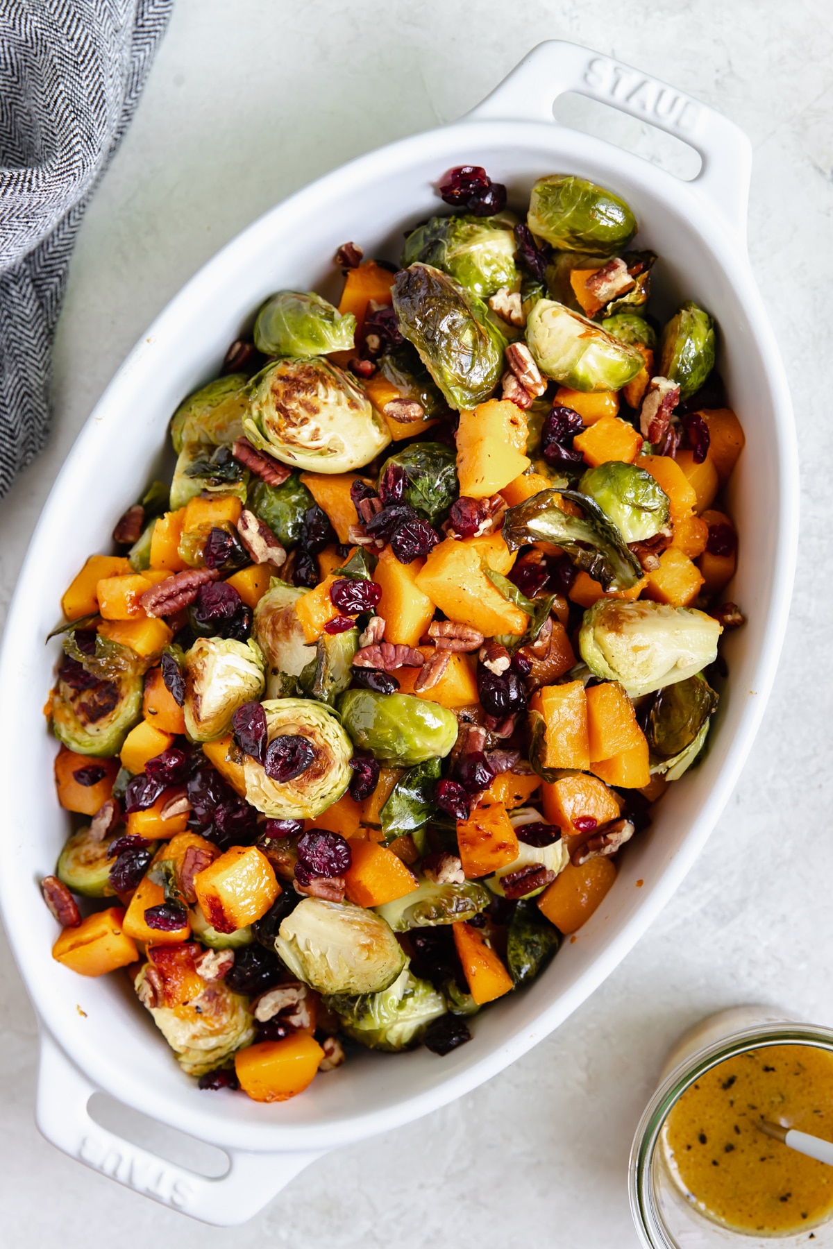 roasted vegetables in a white baking dish garnished with chopped pecans and dried cranberries