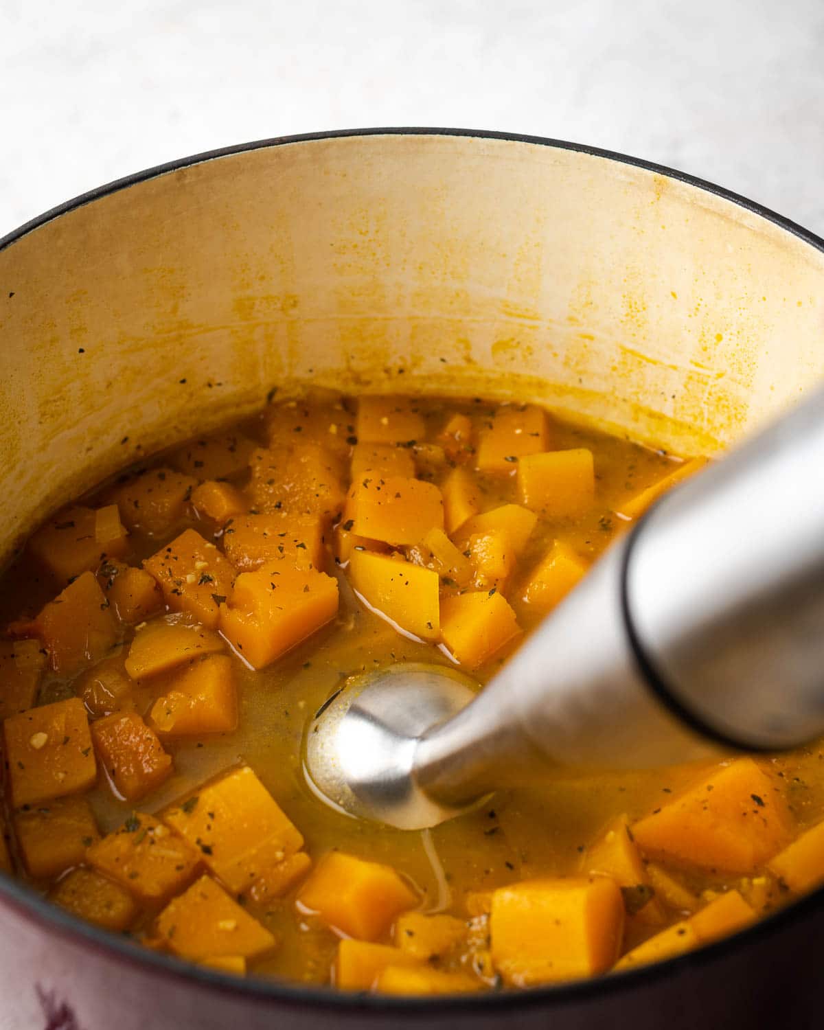 an immersion blended in a pot filled with butternut squash