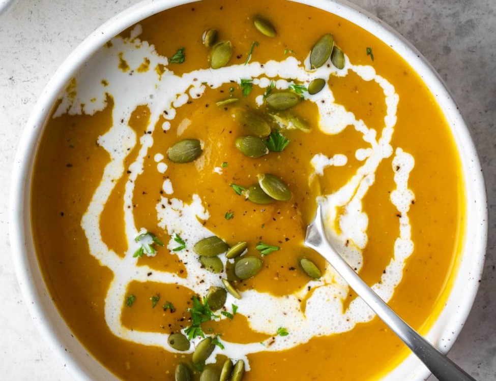 butternut squash soup in a white bowl garnished with heavy cream and pepitas