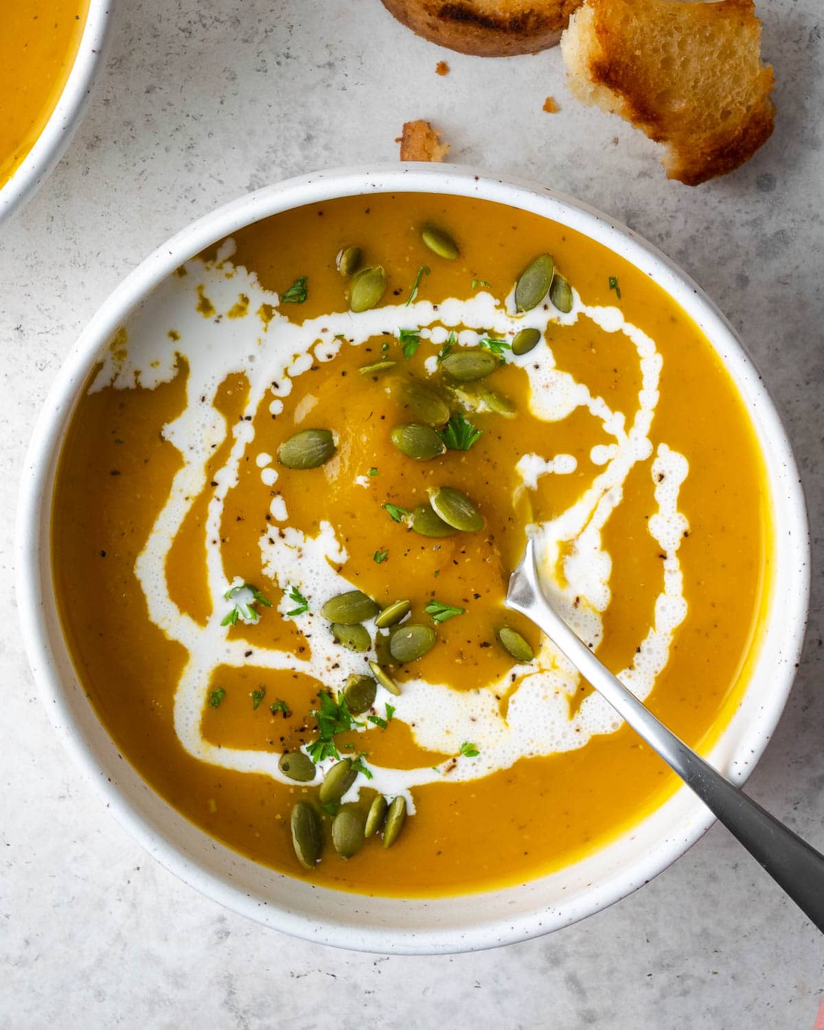 butternut squash soup in a white bowl garnished with heavy cream and pepitas