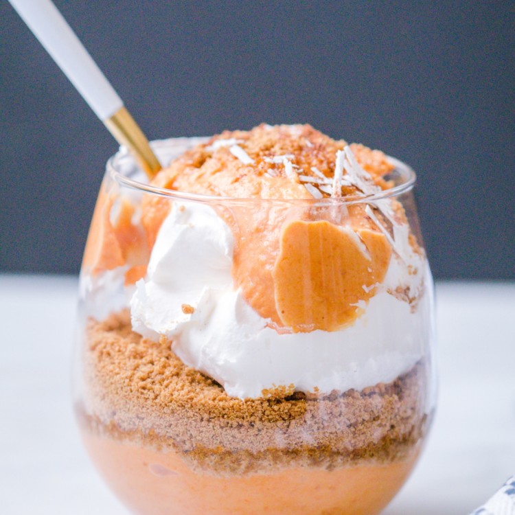 Pumpkin pie parfait layered with pumpkin pie yogurt mixture, ginger snap cookies and cool whip in a wine glass.