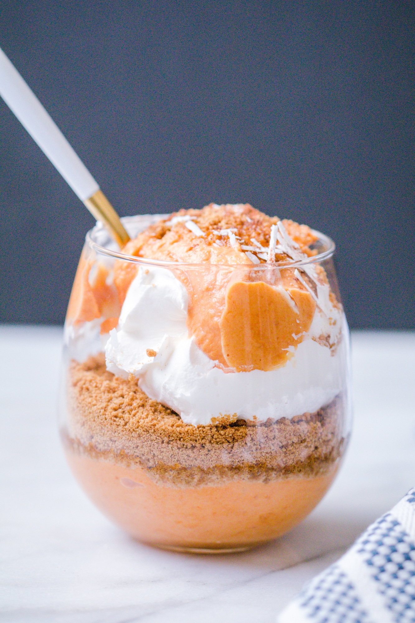 Pumpkin pie parfait layered with pumpkin pie yogurt mixture, ginger snap cookies and cool whip in a wine glass.