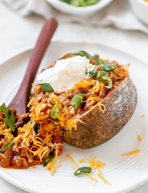 a baked potato filled with sloppy joe meat sauce and garnished with green onions, cheese and sour cream