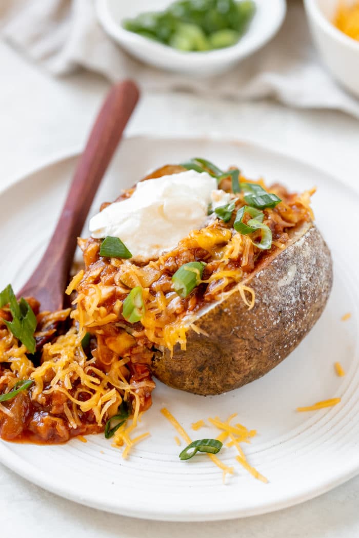 a baked potato filled with sloppy joe meat sauce and garnished with green onions, cheese and sour cream