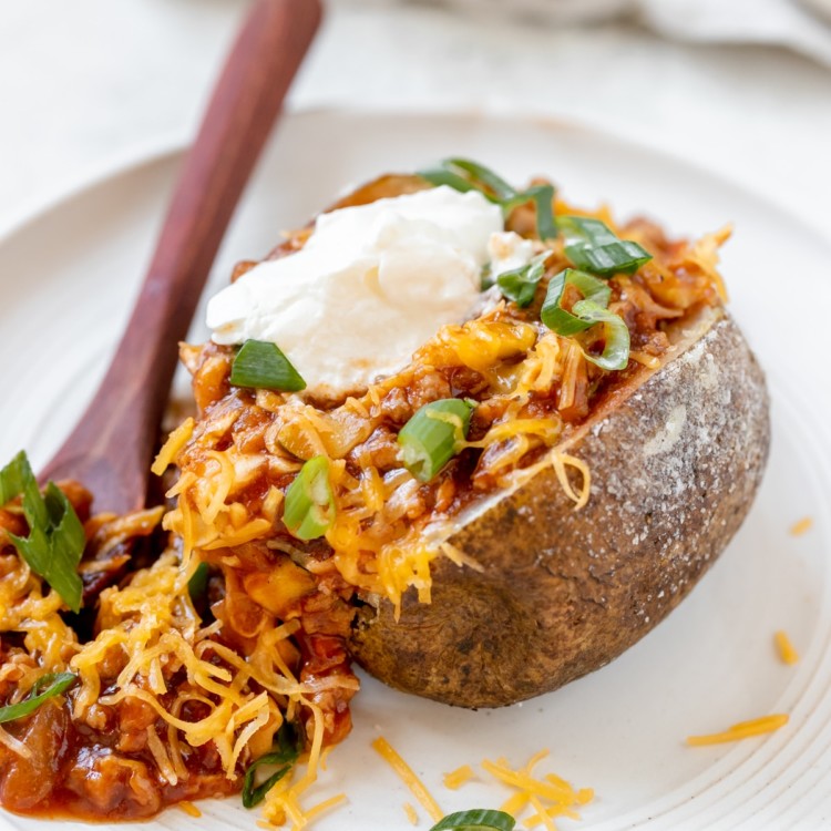 a baked potato filled with sloppy joe meat sauce and garnished with green onions, cheese and sour cream