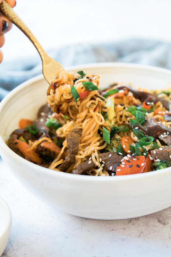 beef and veggie stir fry with a gold fork in a white bowl