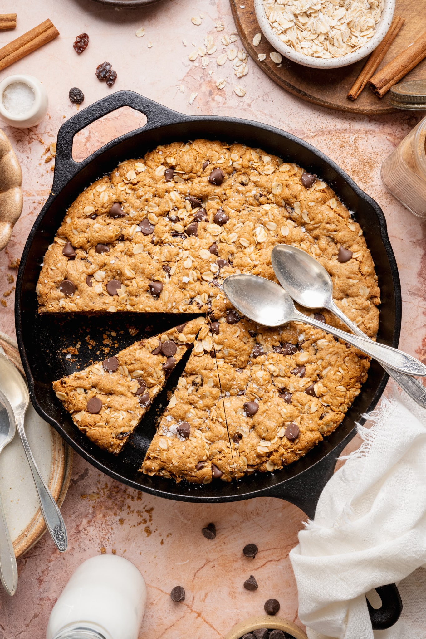 An overhead view of an oatmeal raisin chocolate chip cookie skillet with several slices cut out, revealing a soft center and chewy texture inside the cast iron pan.