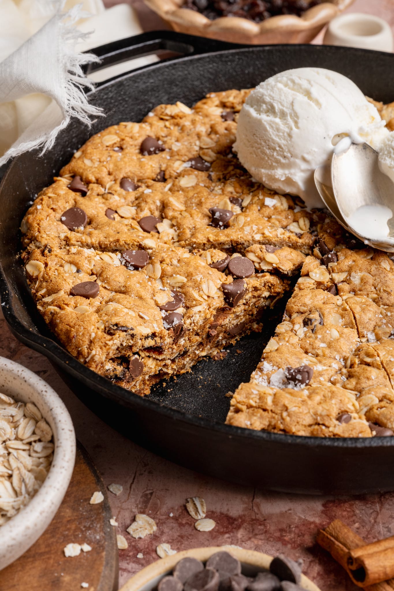 A close-up of an oatmeal raisin chocolate chip cookie skillet topped with a scoop of vanilla ice cream, showing melted chocolate chips and a soft, chewy crumb.