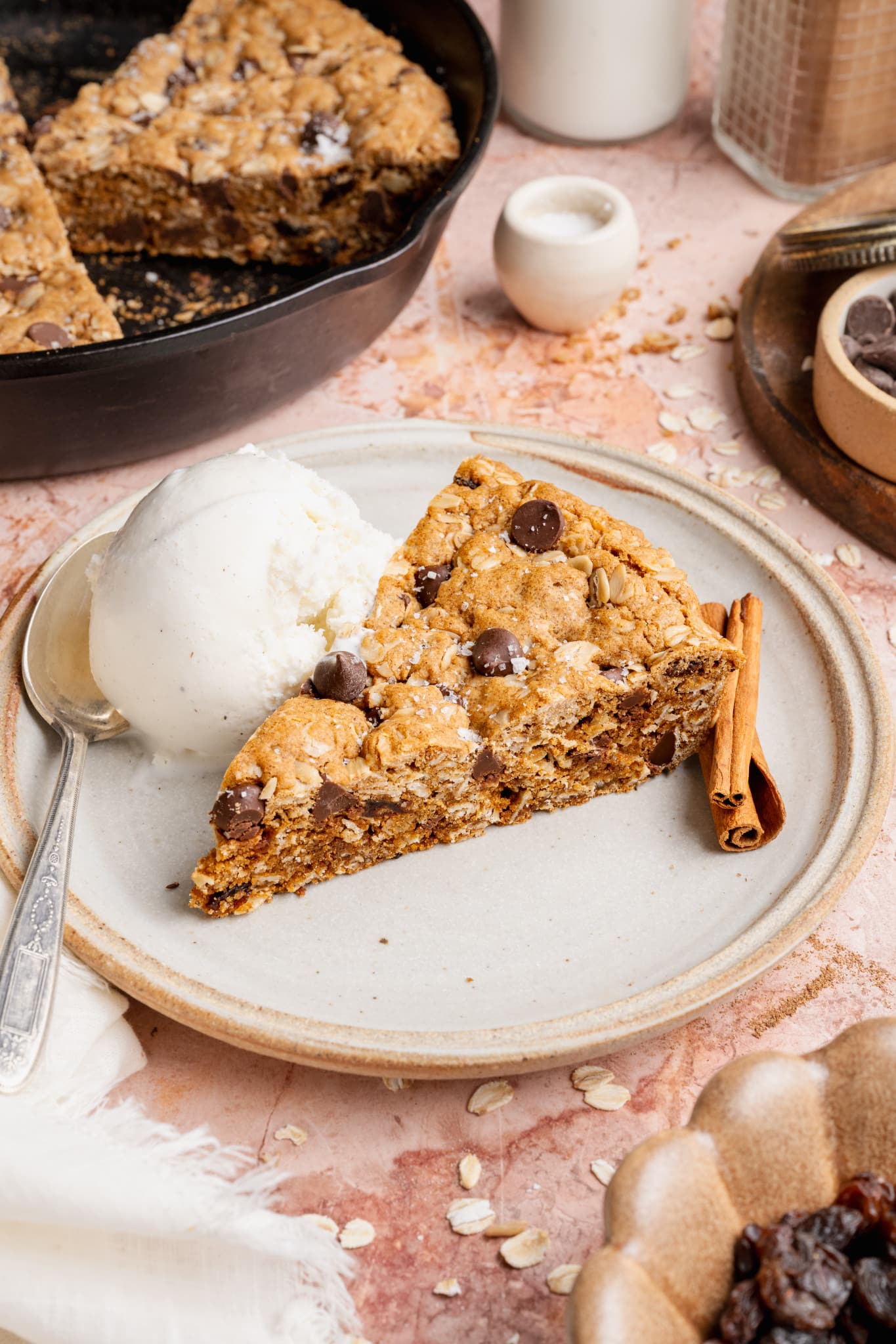 A plated slice of oatmeal raisin chocolate chip cookie served with vanilla ice cream and cinnamon sticks, highlighting the thick, chewy texture of the cookie.