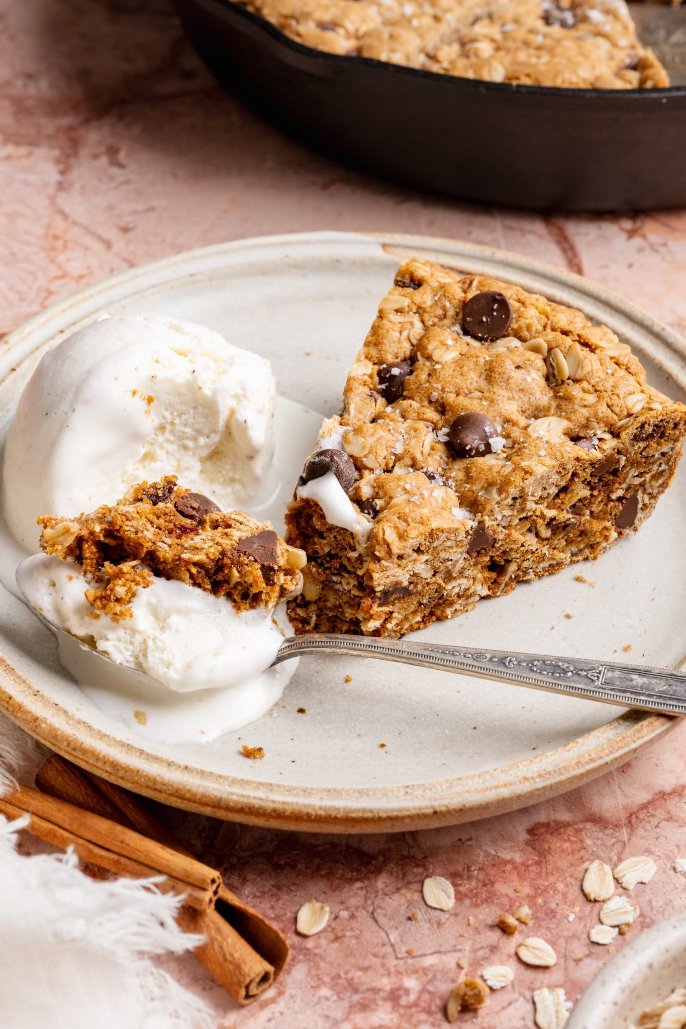 A close-up of a fork cutting into a slice of oatmeal raisin chocolate chip cookie with vanilla ice cream, showing a gooey center and melty chocolate chips.