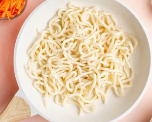 Udon noodles cooking in a skillet with a small amount of water, showing the noodles loosening and becoming pliable.