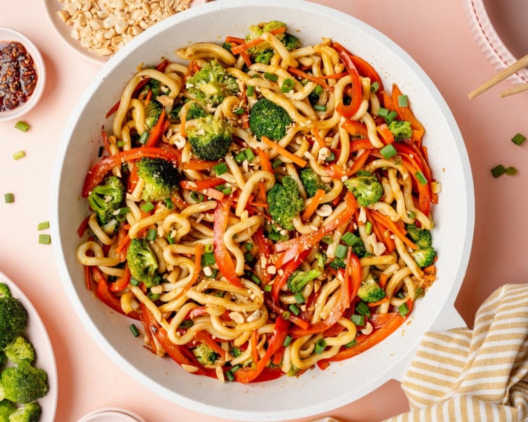 Finished sesame udon noodles tossed together with vegetables, garnished with green onions and chopped peanuts, ready to serve.