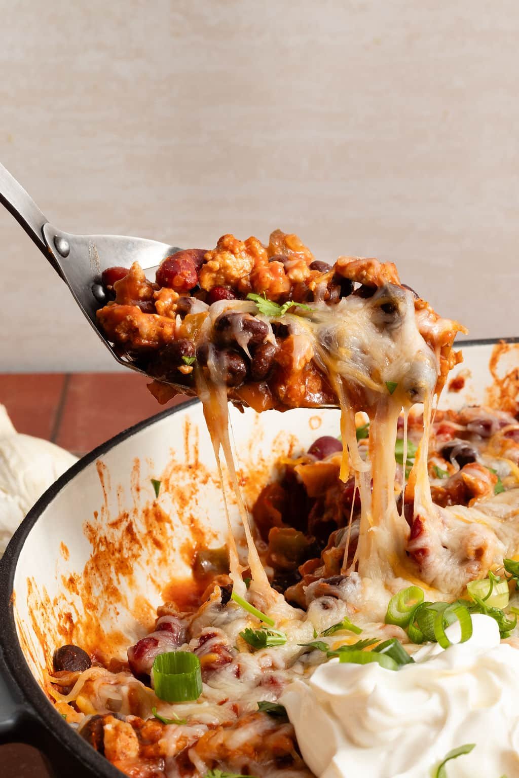 A spoonful of taco skillet being lifted from the pan, showing melted cheese stretching with beans, ground meat, and vegetables.