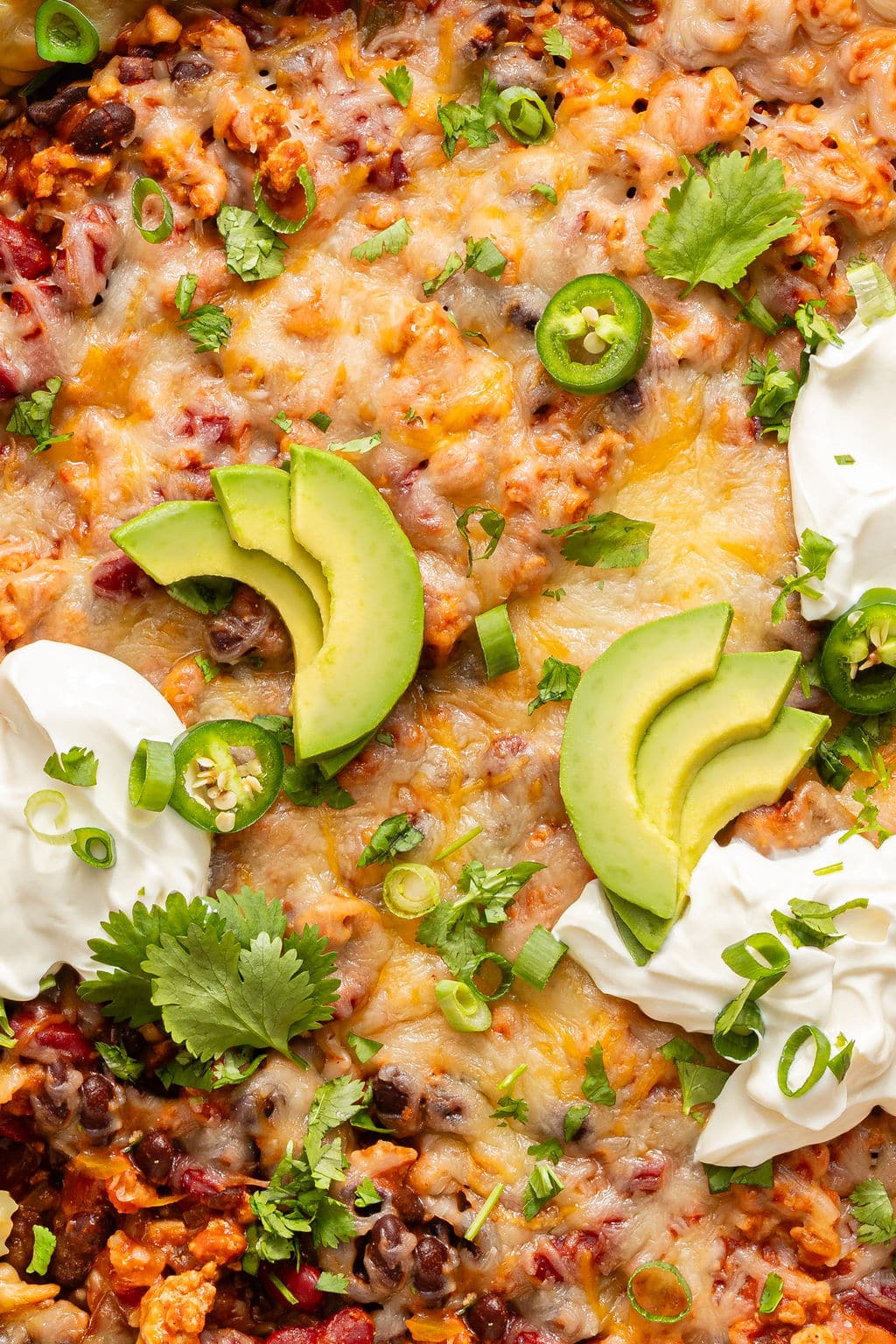 Close-up of the cheesy taco skillet topped with avocado slices, jalapeño rounds, sour cream, and fresh cilantro.
