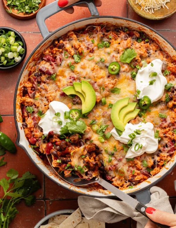 Overhead view of the taco skillet with a serving spoon scooping out a portion, showing melted cheese and hearty filling underneath.